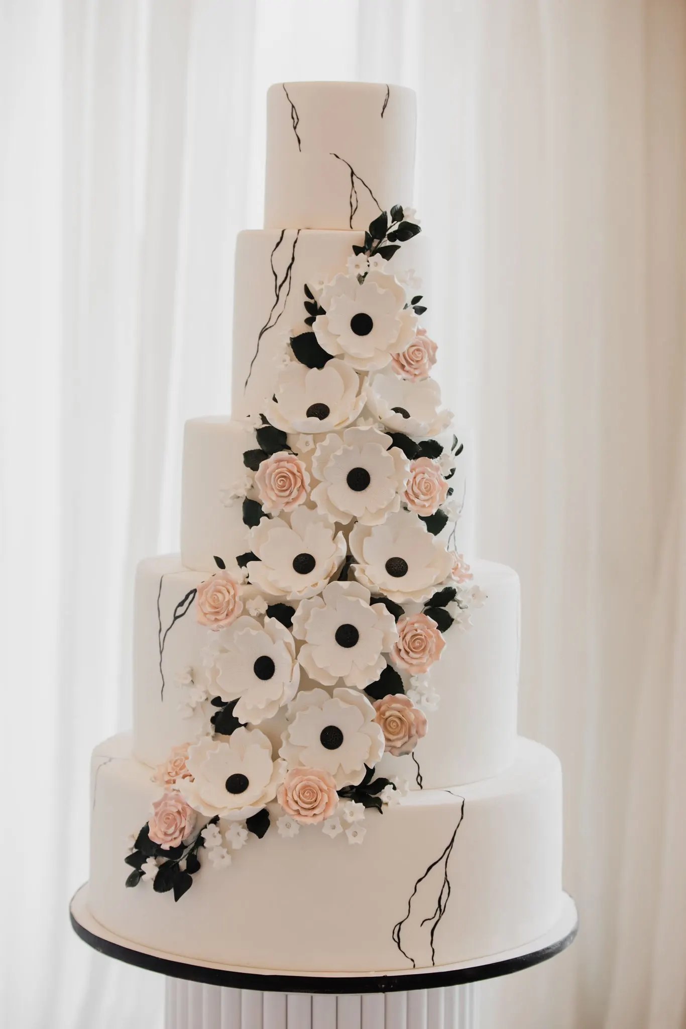 Six-tier white wedding cake with black and blush sugar flowers